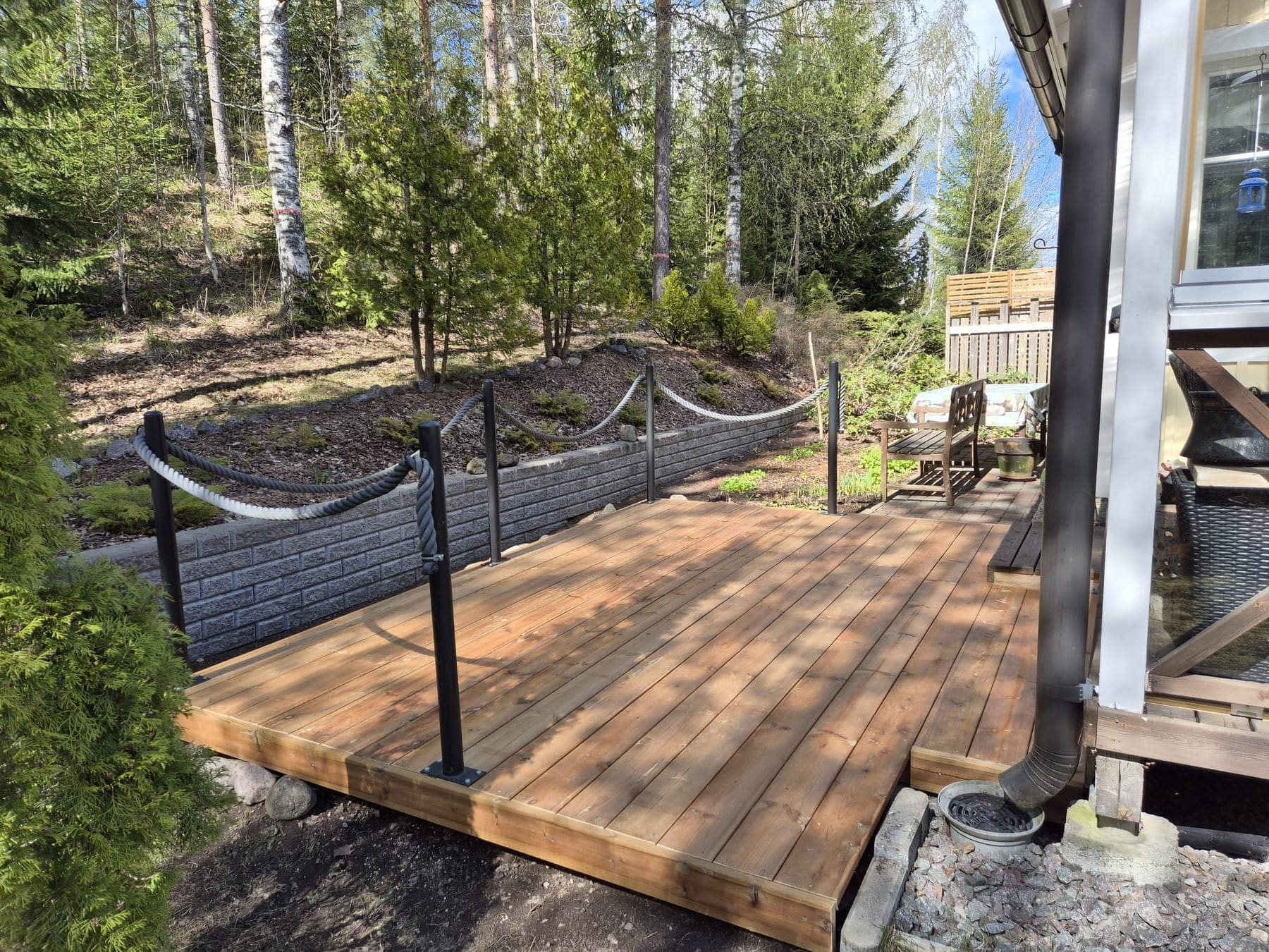 Kevyt puuterassi köysikaiteella metsän laidassa